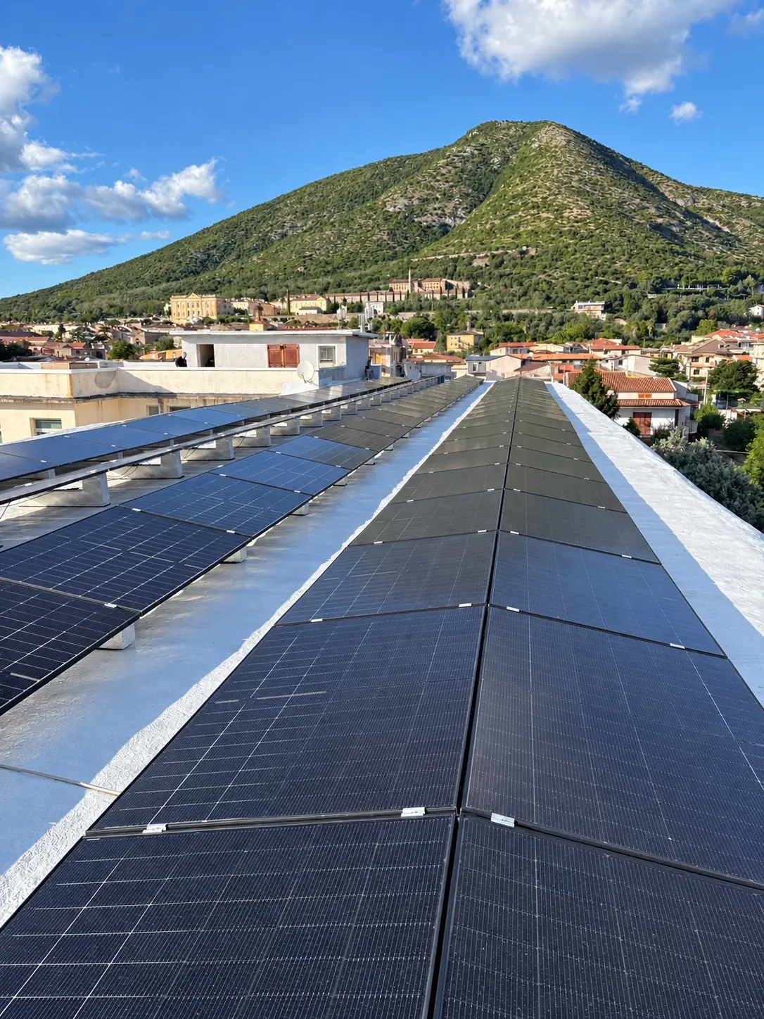 Pannelli fotovoltaici installati su un tetto piano, con la montagna e il paese sullo sfondo