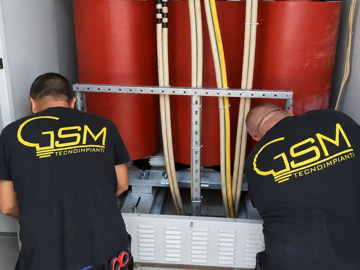 Due tecnici in maglia G.S.M. inginocchiati davanti al trasformatore in resina di una cabina MT/BT