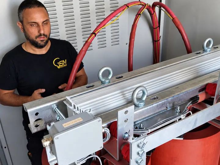 Un tecnico in maglia G.S.M. accanto al trasformatore della cabina, tra sbarre e cavi