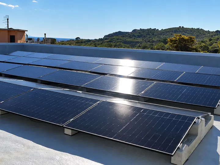 Un campo fotovoltaico su un tetto piano, col sole in controluce e le colline