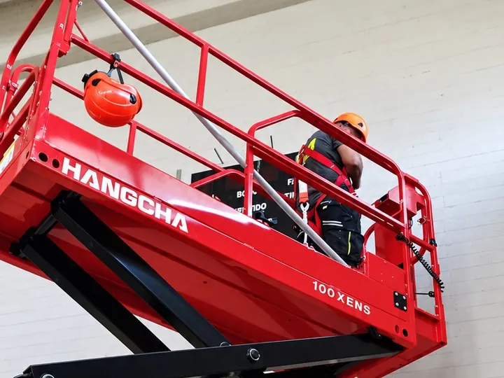 Un tecnico al lavoro sulla piattaforma elevabile rossa, dentro un capannone