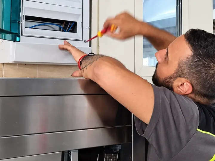 Un tecnico in polo G.S.M. al lavoro sul quadro elettrico di una cucina professionale